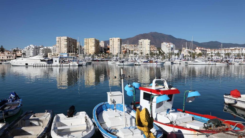 Estepona marina with fishing boats, yachts, and waterfront apartments under a clear blue sky on the Costa del Sol