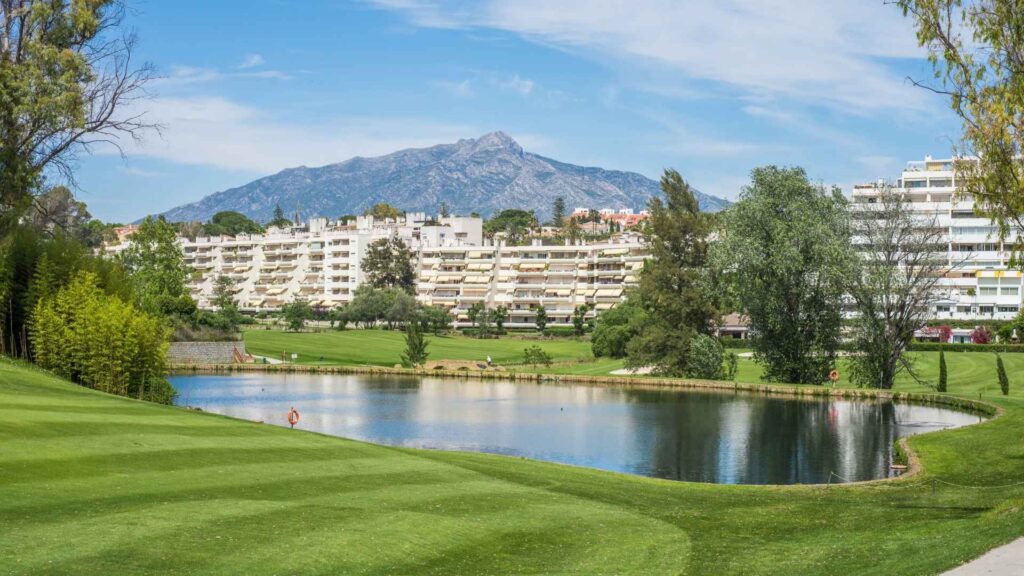 Golf course in Nueva Andalucía, Marbella, with mountain views and residential buildings overlooking a lake on the Costa del Sol.