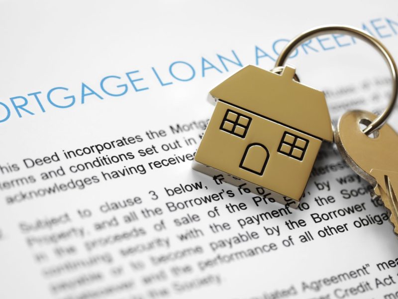 House-shaped keychain and key placed on a mortgage loan agreement document.