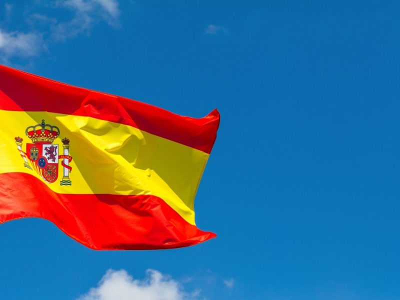 Spanish flag waving against blue sky, symbolizing property investment and real estate opportunities in Spain.